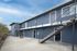 Modern two-story apartment building with stylish blue exterior, featuring sleek metal staircases and a spacious concrete parking area.