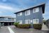 Charming blue apartment complex with modern architecture, surrounded by manicured hedges under a bright blue sky.
