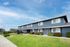 Charming row of modern townhouses with manicured lawns and vibrant blue skies, offering a welcoming community living environment.