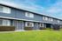 Charming townhouse exterior with modern design, featuring lush green lawn and vibrant landscaping under a bright blue sky.