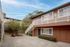 Charming two-story apartment with a cozy outdoor seating area, beautifully landscaped with lush greenery and elegant stairway access.