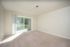 Bright living room with plush carpet and large sliding glass door opening to a lush green outdoor space.