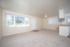 Bright and airy living space with plush carpeting, large windows with blinds, and an open layout leading to the kitchen area.