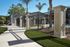 Charming pathway lined with lush greenery, elegant iron fencing, and a welcoming facade basking in sunlight.