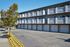 Charming multi-level apartment building with elegant balconies and attached garages, surrounded by a beautifully landscaped street lined with vibrant flowers and trees.