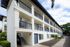 Charming three-story apartment building with elegant balconies, set against a blue sky, surrounded by lush greenery.