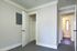 Bright, empty room with plush gray carpet, white trim, and closet space, leading to a hallway with open doors.