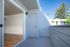 Charming balcony with modern wood flooring opening to a sunlit, spacious interior, surrounded by lush greenery and clear blue skies.
