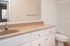 Bright and modern bathroom with elegant beige countertop, large mirror, and pristine white cabinetry, perfect for a serene home retreat.