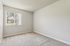 Bright and inviting empty room with soft carpet, large window, and modern gray walls, offering ample natural light and a cozy atmosphere.