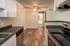 Elegant kitchen with modern appliances and warm wooden flooring, leading to a spacious and well-lit area with contemporary ceiling fan.