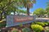 Inviting entrance to Sandpiper Village with lush landscaping and towering palm trees, offering a serene residential community vibe.