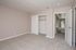 Bright and airy bedroom with neutral walls, plush carpet, and a spacious closet featuring sliding doors. Open door leads to a sunlit corridor that enhances the inviting ambiance.