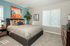 Charming bedroom with a modern design, featuring a plush bed, vibrant artwork, and abundant natural light through wide windows.