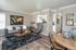 Bright and inviting living room with modern decor, featuring a stylish gray sofa, unique wall art, and an elegant wooden coffee table on a plush rug. Open-concept design with a glimpse into the sleek kitchen area.