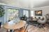 Inviting open-concept living room with stylish decor, featuring a cozy sofa, elegant armchair, rustic coffee table, and lush greenery by a large, sunlit window.