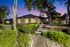 Charming single-story home nestled in lush greenery with a welcoming pathway, beautifully lit at dusk.