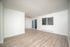 Bright and spacious living area with elegant wood flooring, large window, and sliding glass door leading to a serene outdoor view.