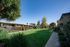 Charming apartment complex with vibrant green lawns, wooden fences, and lush trees under a clear blue sky.