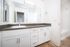 Modern bathroom with sleek white cabinets, elegant countertop, large mirror, and wood flooring.
