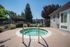 Inviting outdoor spa area with a sparkling round hot tub surrounded by lush greenery and a sunny, clear blue sky.