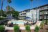 Charming apartment complex featuring a sunlit pool area surrounded by lush greenery and modern lounge furnishings, perfect for relaxation.