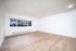 Bright and spacious empty living room with large window, showcasing elegant wooden flooring and freshly painted white walls.