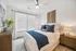 Elegant bedroom with modern decor, featuring a plush bed with blue accents, stylish artwork, and warm natural light streaming through large windows.