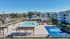Luxurious apartment complex featuring a sparkling pool, elegant clubhouse, and tennis court set amidst landscaped gardens.