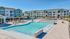 Modern apartment complex with a large, inviting swimming pool surrounded by sun loungers and pergolas, set against a backdrop of stylish, multi-story residential buildings.