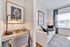 Chic apartment interior with a cozy white sofa, decorative pillows, modern artwork, and a stylish small study nook featuring a sleek lamp and granite desk.
