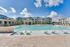 Luxurious apartment complex featuring a sparkling pool with lounge chairs, surrounded by modern buildings under a bright blue sky.