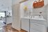 Bright utility area featuring modern washer and dryer with open shelving, adjacent to a stylish kitchen and inviting living space.