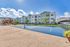 Modern apartment complex with a pristine tennis court and lush landscaping under a bright blue sky.