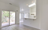 Bright apartment interior featuring an open layout with large windows, sleek sliding glass doors to a balcony, and a modern kitchen with a high counter.