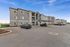 Modern apartment complex with stylish exterior, ample parking, and beautiful landscaping under a bright blue sky.