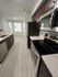 Modern kitchen with sleek stainless steel appliances, dark wood cabinetry, and stylish light-colored flooring leading to a bright dining area with large windows.