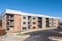 Modern three-story apartment building with brick and stone facade, featuring private balconies and ample parking.