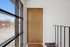 Inviting apartment entrance with a wooden door and large sunlit windows offering charming outdoor views.