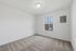 Bright and spacious room with soft carpet flooring, pristine white walls, and a window allowing ample natural light.