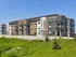 Modern multi-story apartment complex with sleek facade design, large windows, and balconies, set against a clear blue sky.