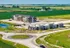 Modern apartment complex surrounded by lush green fields with nearby commercial spaces and roundabout access.