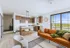 Bright and modern open-concept living space with a stylish kitchen, sleek bar stools, and a cozy seating area overlooking scenic views.
