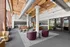 Modern communal space with high ceilings, industrial-style beams and exposed ductwork, featuring cozy seating areas, vibrant chairs, and a stylish kitchenette.