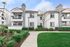 Charming Mediterranean-style apartment building with lush landscaping and a clear blue sky.