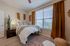 Charming bedroom with cozy bed, stylish decor, large window with ample natural light, and warm wooden flooring.