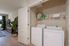 Modern apartment interior showcasing an in-unit laundry area with washer and dryer, adjacent to a stylish living space with large potted plants and elegant decor.