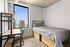 Modern bedroom with single bed and cozy workspace, offering stunning cityscape views through a large window.