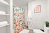 Bright and charming bathroom featuring a colorful floral shower curtain, elegant shelving with pristine towels, and a vibrant wall art piece with 'Take It Easy' message.
