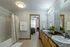 Bright and spacious bathroom featuring double sinks, modern lighting, and elegant decor with a view into a cozy bedroom.